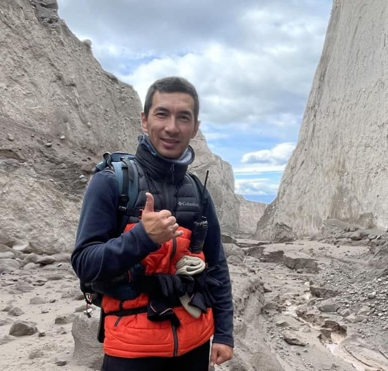 A man in hiking gear gives a thumbs-up gesture in a rocky canyon landscape.