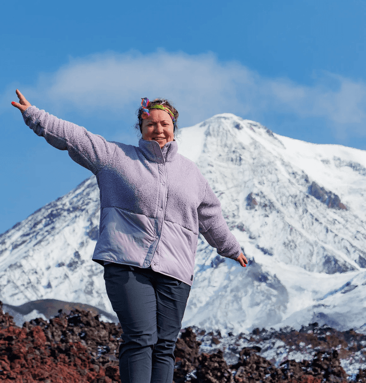Smiling woman with outstretched arms in front of a majestic snow-capped mountain.