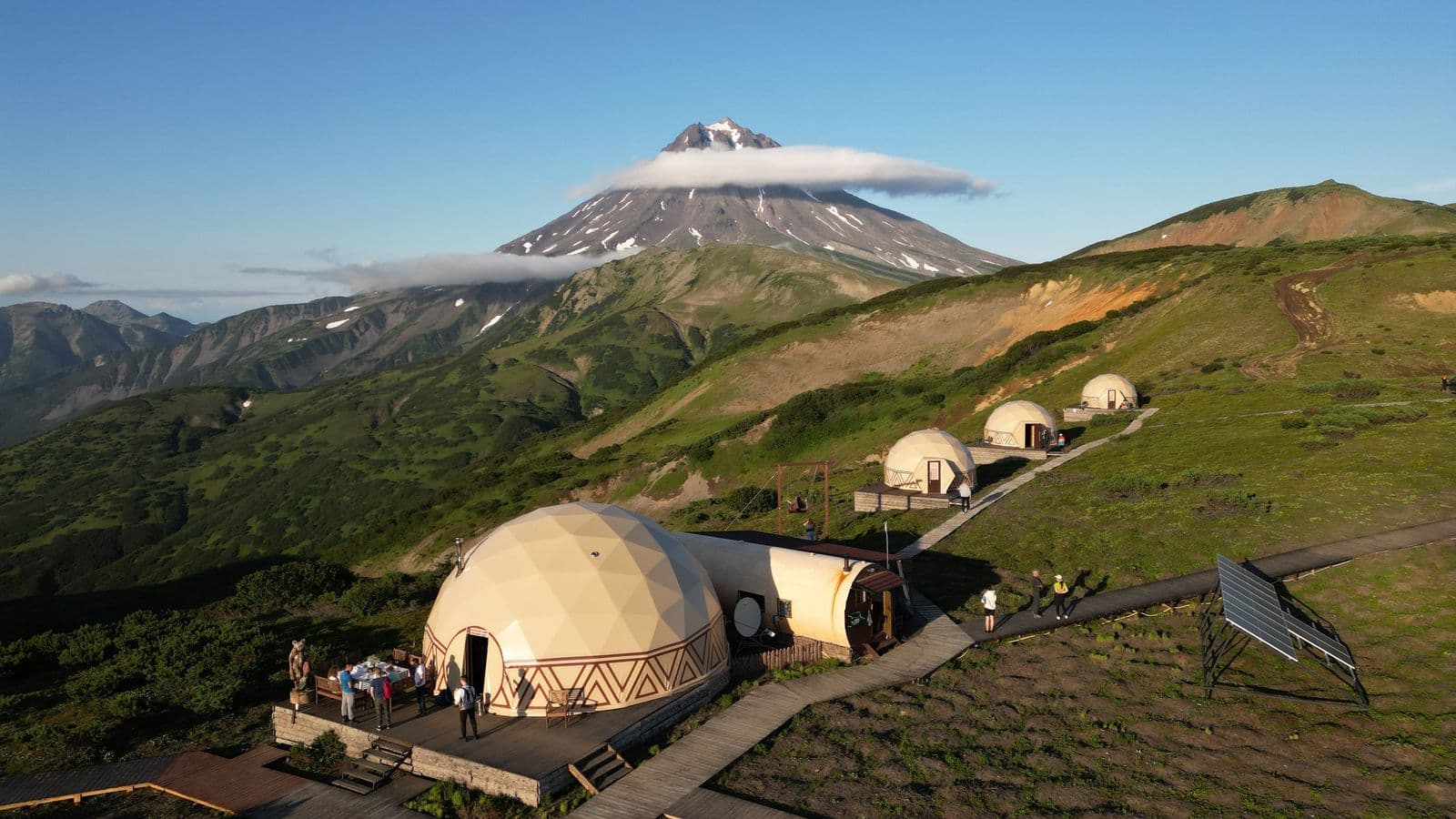 Geodesic domes nestled on a green hillside with a cloud-capped mountain in the background.
