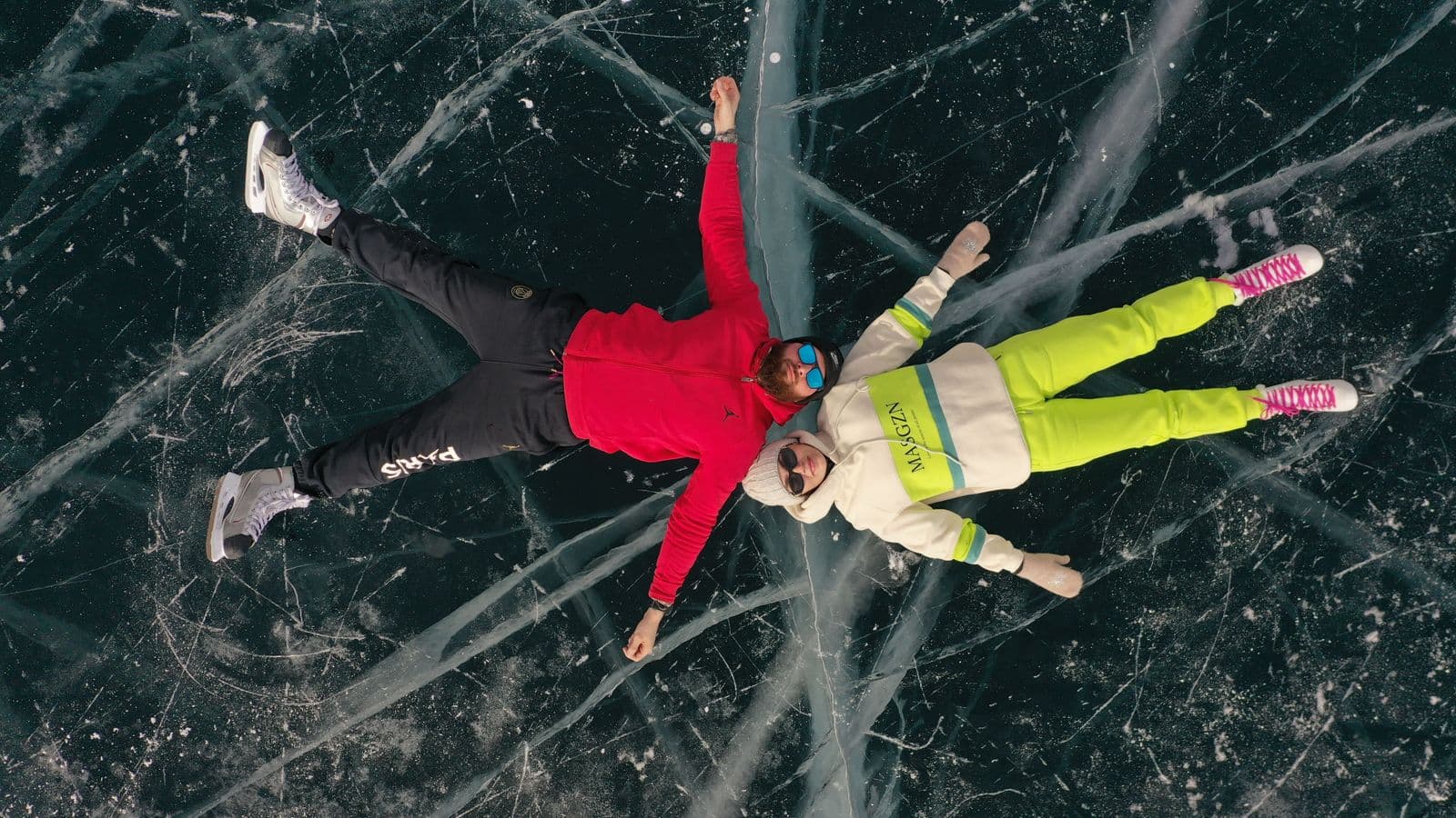 Overhead view of two ice skaters lying spread-eagled on a beautiful cracked frozen lake.