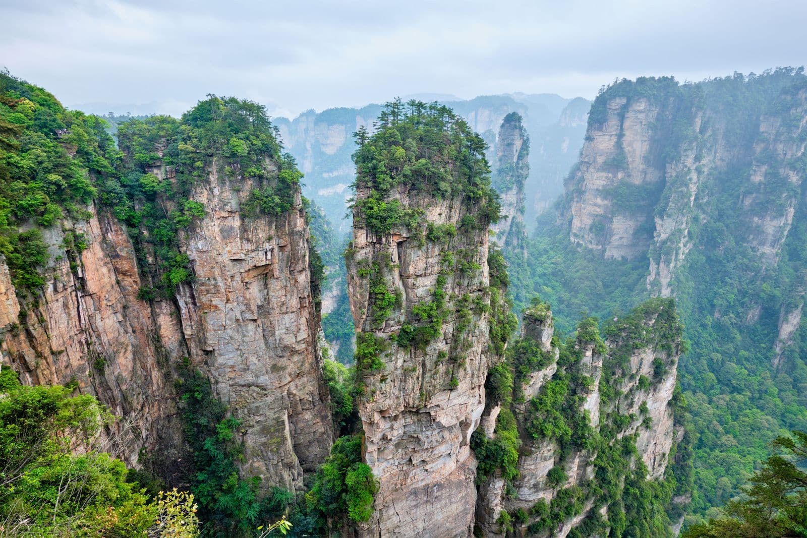 Tall, mist-shrouded rock pillars covered in green vegetation in a mountainous landscape.