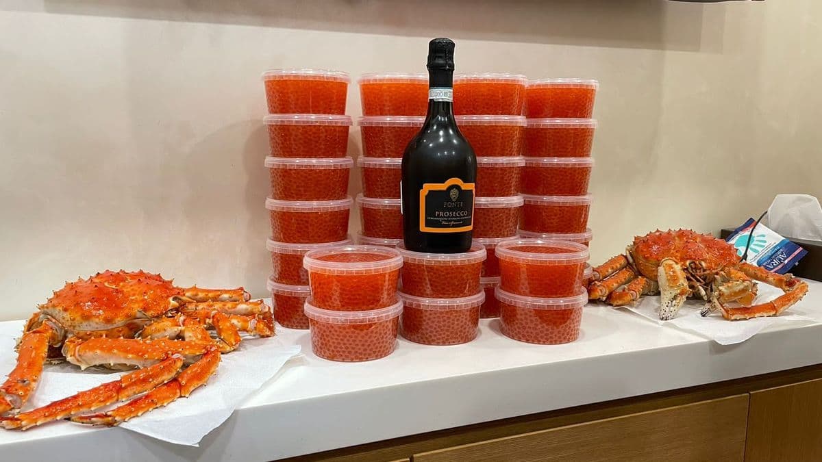 Two cooked King crabs flank a dark bottle surrounded by stacks of red caviar containers.