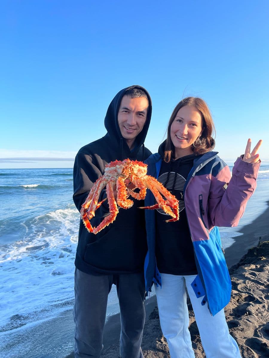 A man and woman proudly display a large king crab on a sunny beach.
