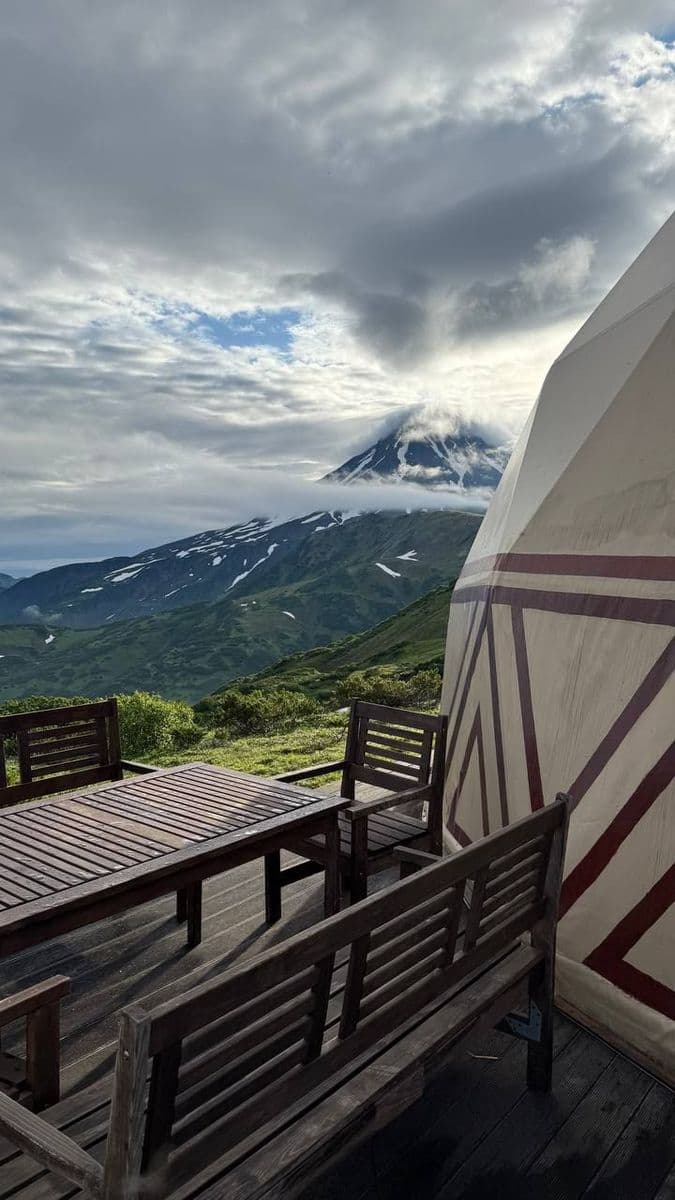 Outdoor patio and glamping dome facing a cloud-covered, snow-capped mountain.