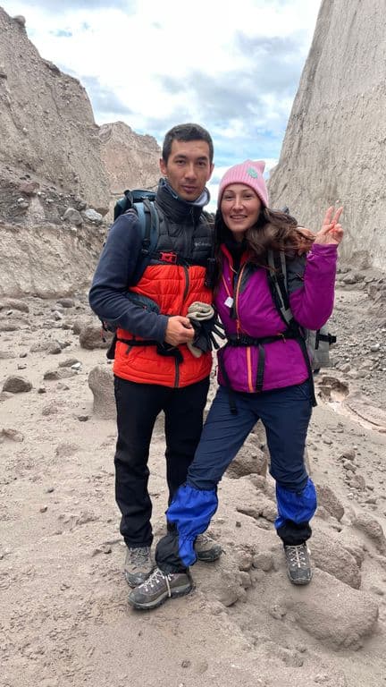Two smiling hikers in outdoor gear pose against a backdrop of towering rocky canyons.