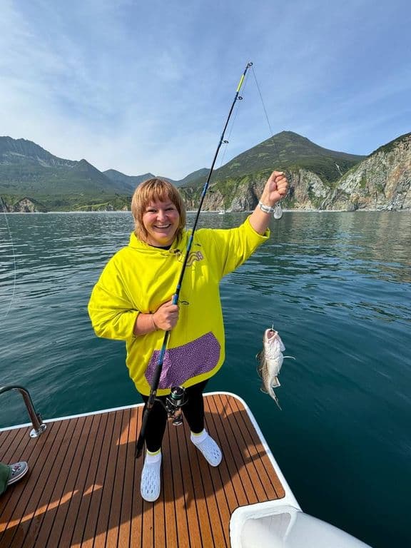 Happy woman on boat holds fishing rod with freshly caught fish.